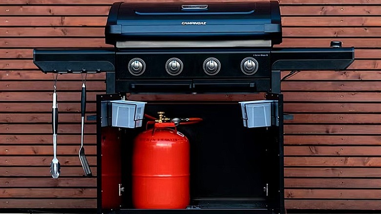 A black gas-powered grill next to the side of a house
