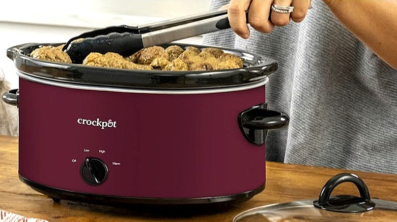 Close-up of a person's hand using tongs to remove food from a Crock-Pot