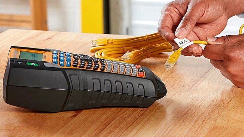 A black label maker sitting on a table while a person labels some cord