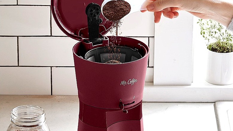 Close-up of a hand pouring in coffee beans in a burgundy coffee maker