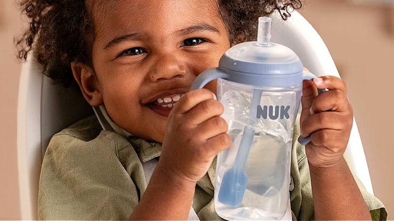 A smiling baby holding a Nuk water bottle