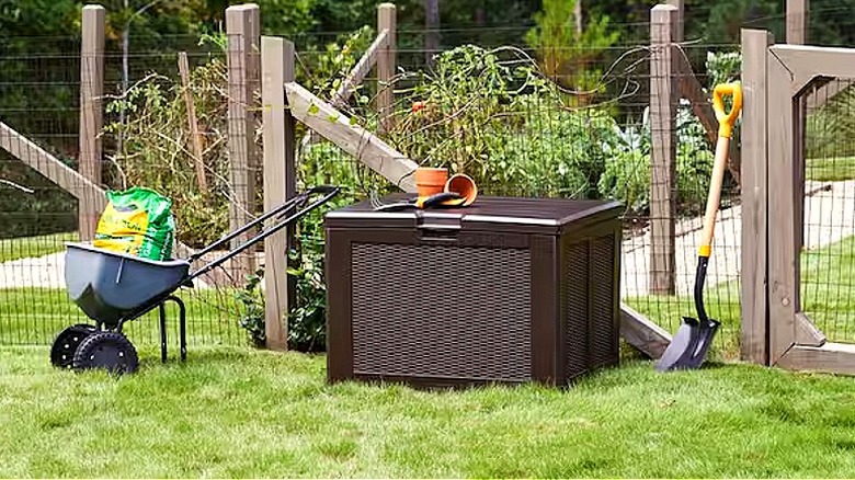 A brown outdoor storage deck box sitting in a yard with two pots on top