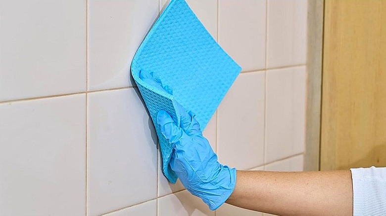 Hand using a blue sponge cloth to clean bathroom wall tiles
