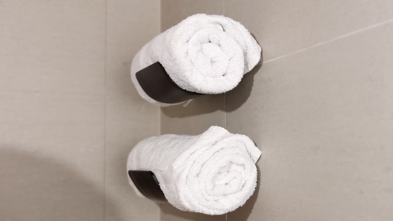 Two white towels rolled up on black towel holders mounted to the wall