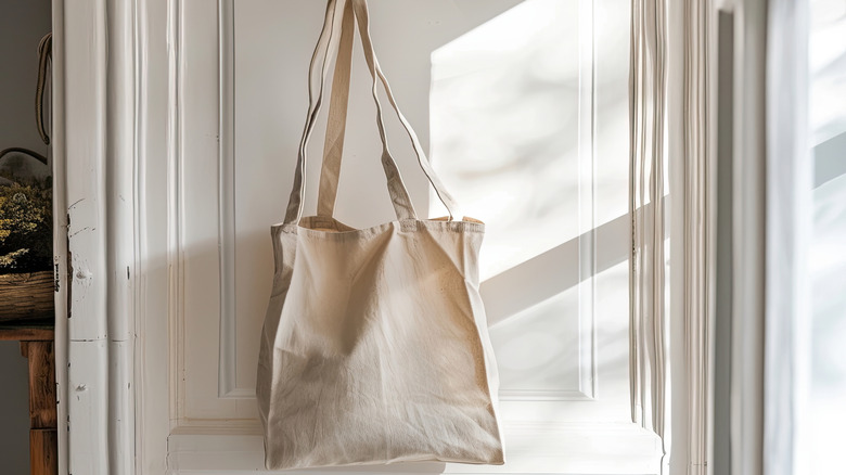 tan tote bag hanging on white door in home