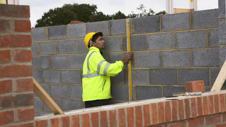 A person leveling a wall made of cinderblocks with bricks in the foreground