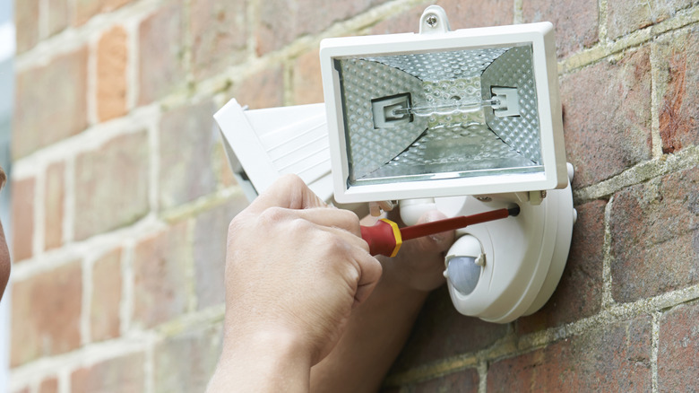 Hands installing a white flood light to a house's exterior
