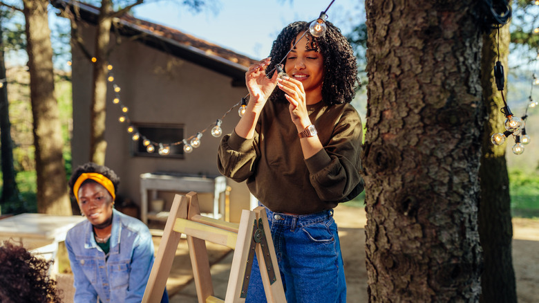 A woman hanging string lights outdoors