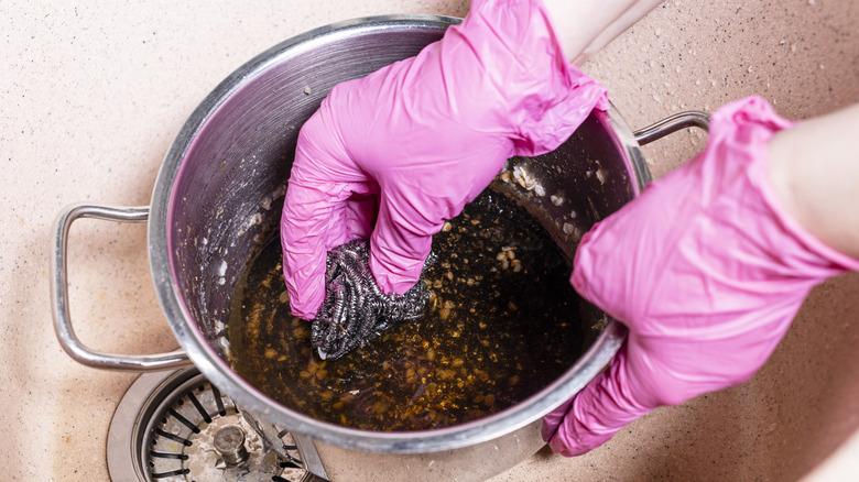 A person wearing pink gloves scrubbing a burnt pot in a sink