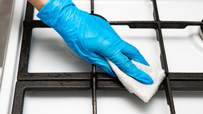 Someone wiping the stove grates with a white cloth