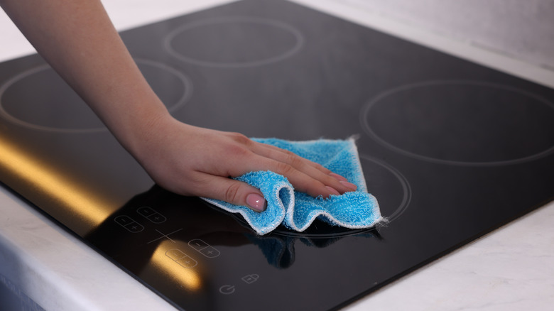 A person cleans the glass surface of an induction cooktop with a blue rag.