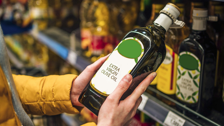 A person picking up a bottle of olive oil at the grocery store