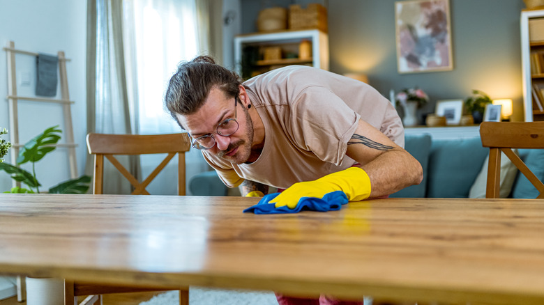 A person wiping a wood table with a clean cloth