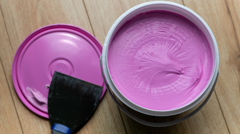 An opened tub of pink spackle with the lid sitting next to it