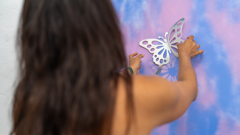 A woman using a butterfly stencil on a canvas on a wall