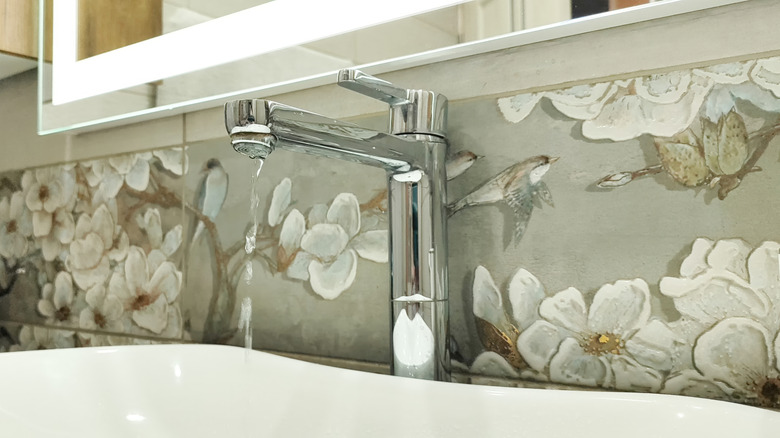 Close-up of a stainless steel faucet and a floral painted tile backsplash