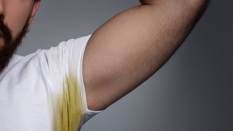 Man lifting arm showing yellow stain on white shirt.
