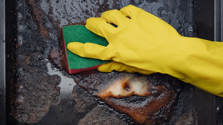 rubber gloved hand scrubbing dirty baking sheet