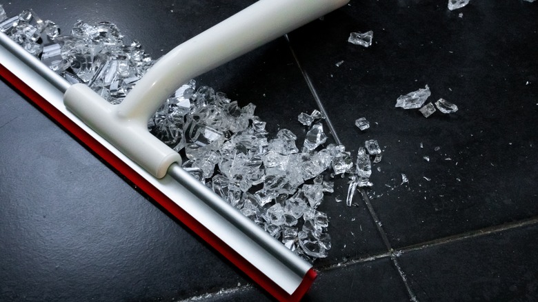 Using squeegee to clean broken glass on black flooring