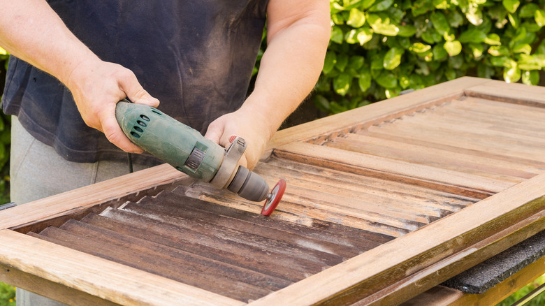 A person sands a wooden shutter outside.