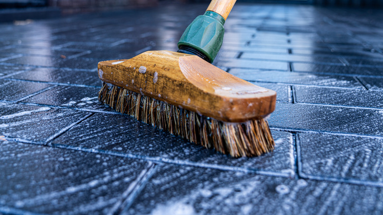 A red and black broom lies on a wood floor covered in soapy water.