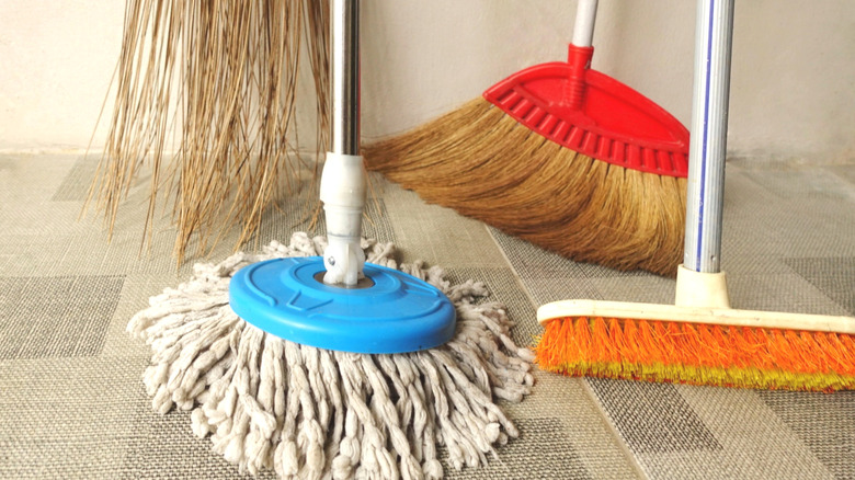Three brooms and a mop on a woven fabric floor.