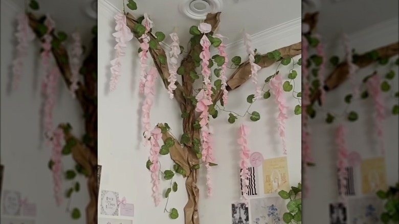 The corner of a bedroom decorated with a tree made from brown paper and pink hanging tissue flowers