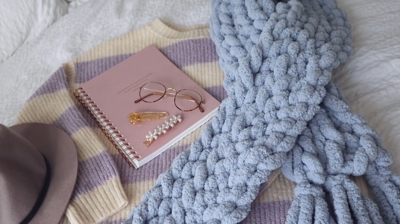 A thick blue scarf over a top and near a notebook