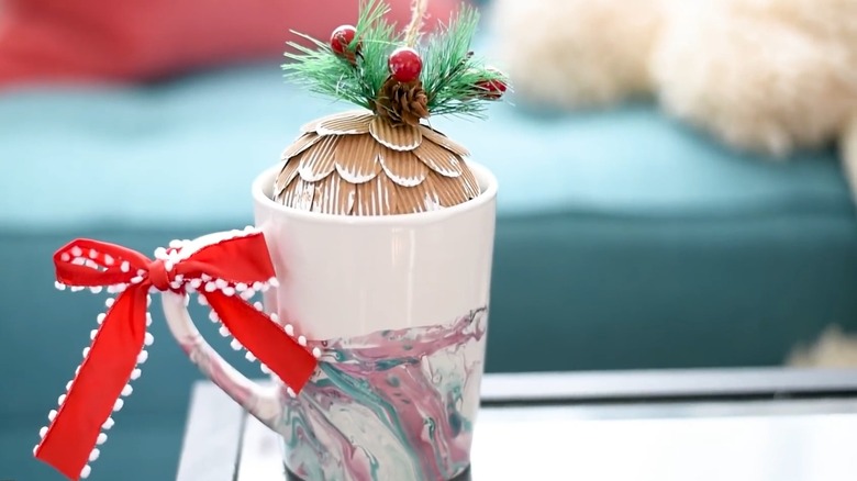 A white coffee mug with marble design, a red bow, and a Christmas ornament