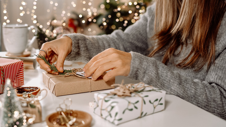 Woman wrapping gift using brown paper and winter foliage
