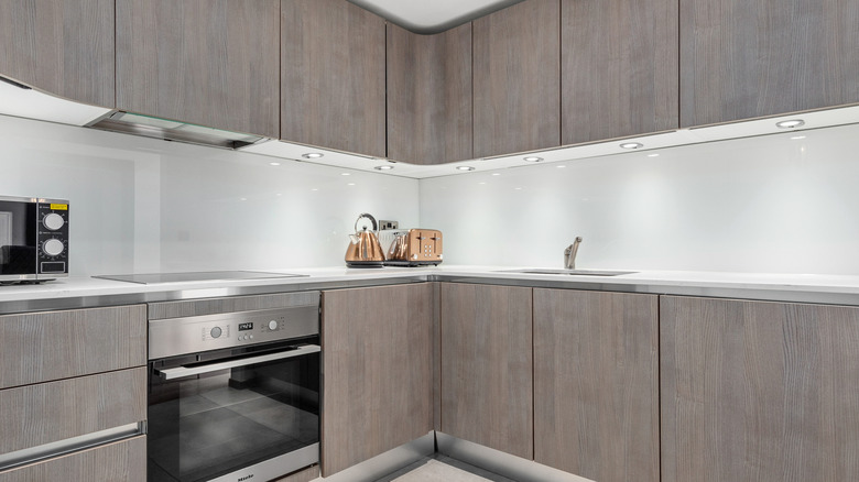 A brightly lit kitchen with grey cabinetry and a shiny white backsplash.