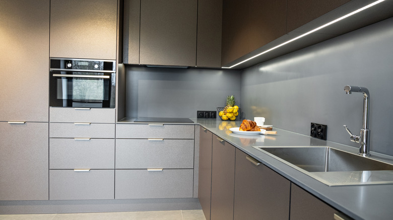 A modern kitchen with linear lighting under the cabinets and a sleek, plain grey backsplash.