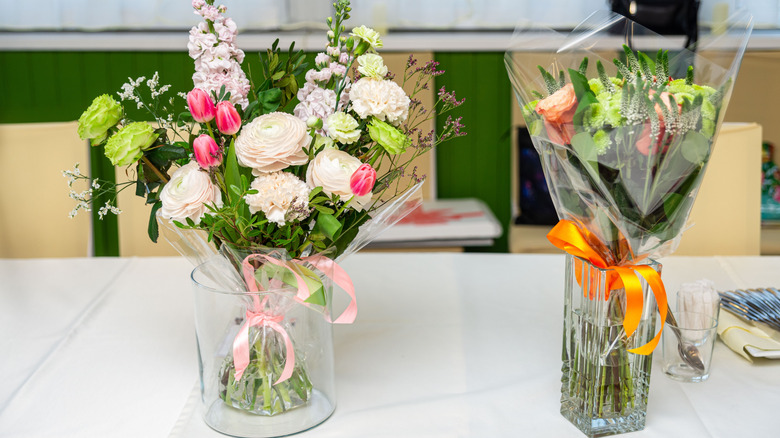 A pair of pretty glass vases sitting on a white counter top and filled with floral bouquets