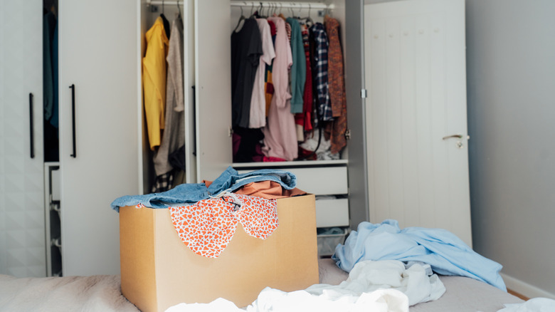 A box on the bed with clothes inside and an open closet behind.