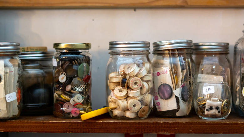 Glass mason jars used to store buttons on a wooden shelf.