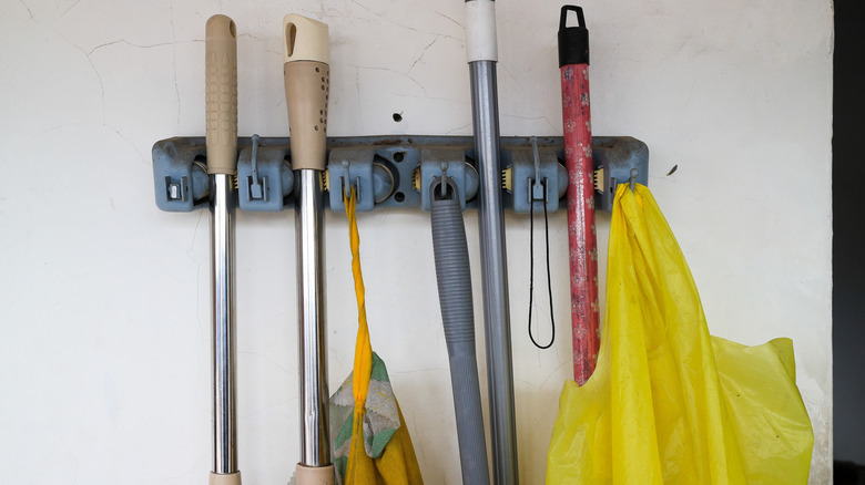 A wall-mounted broom holder with multiple brooms hanging on it.