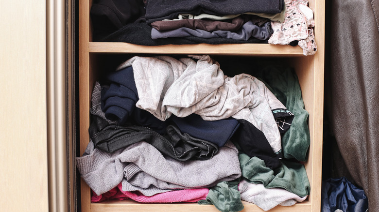 A close-up of a closet with cubby shelving packed with disorganized clothes.