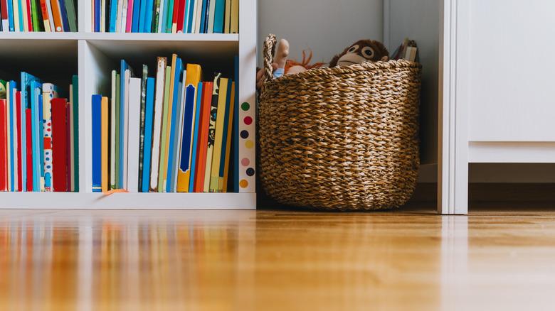 A wicker basket used to store toys in between a white cabinet and a bookcase.