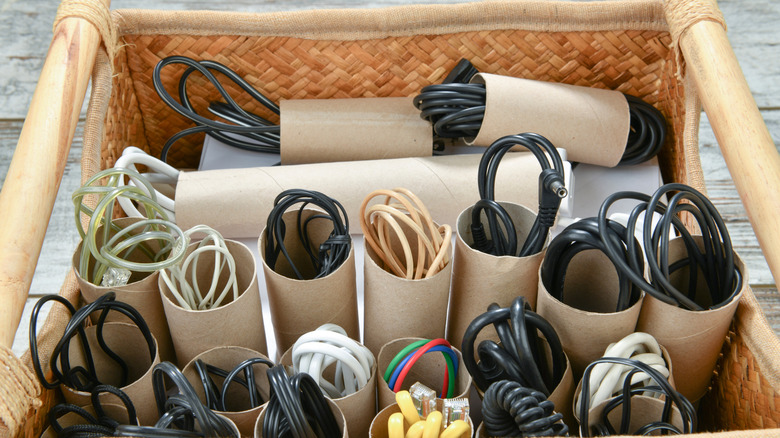 Various electric cords organized with empty toilet paper rolls in a woven basket.