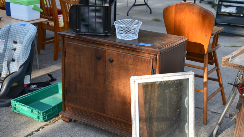 Yard sale with a wooden accent cabinet, storage baskets, and a wooden high chair.