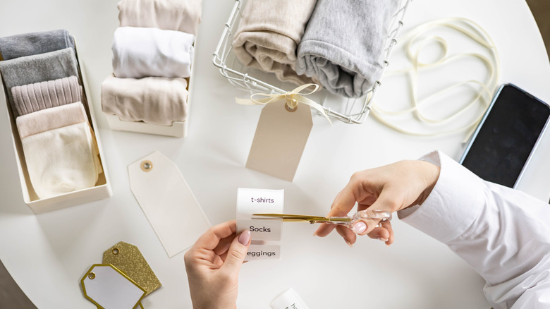 Person's hands cutting labels for baskets to store t-shirts, socks, and leggings.