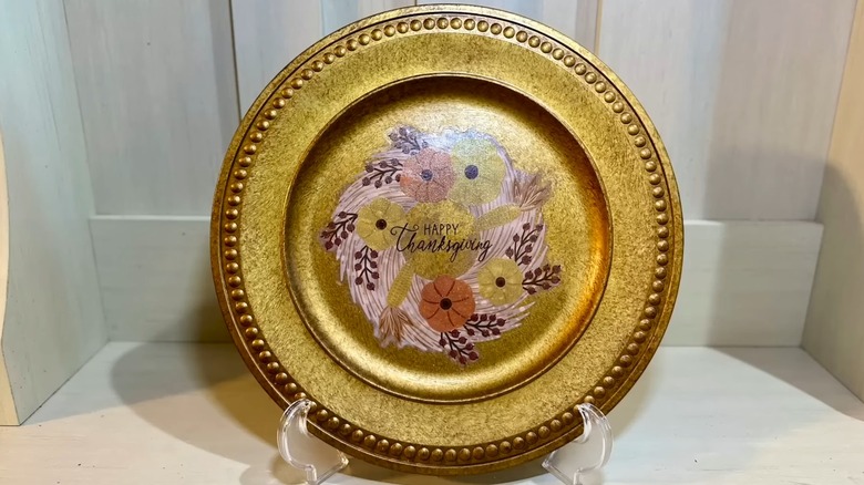 A gold charger plate with a Thanksgiving motif on top