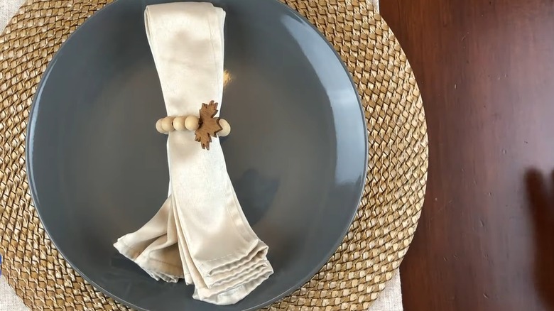 A wooden bead napkin ring holding a white napkin over a plate