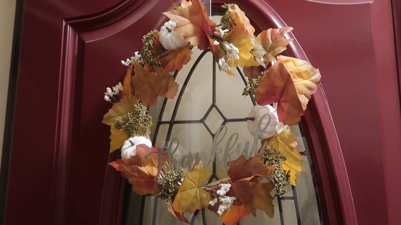 A fall wreath including leaves and pumpkins on a front door