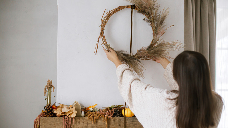 Woman hanging an autumnal wreath over a fireplace
