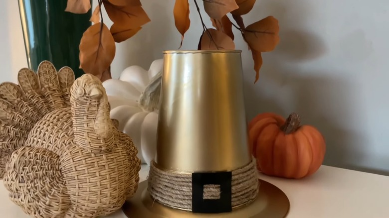 A golden pilgrim hat surrounded by pumpkin and turkey decor pieces