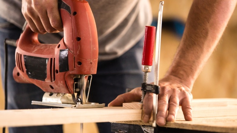 person cutting wood board with jigsaw