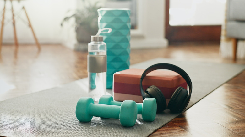 Weights, headphones, and water bottle with other gym equipment on yoga mat