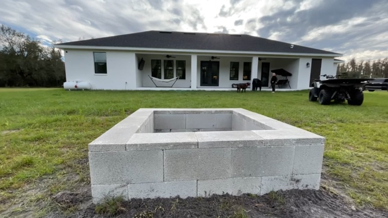 A newly built concrete cinder block fire pit in the yard outside a white house.