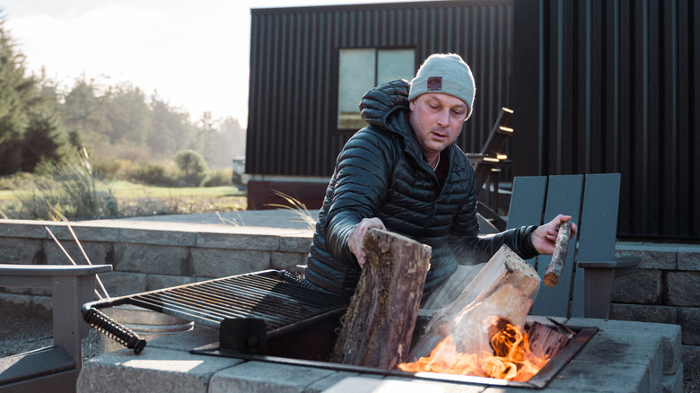 Man placing wood into a square concrete fire pit in backyard.